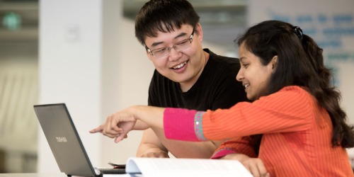 Two students, looking at a laptop as they study together.